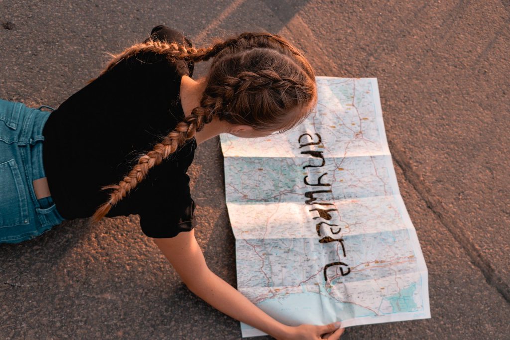 Jeune fille allongée sur une route qui regarde une carte du monde où est écrit anywhere
