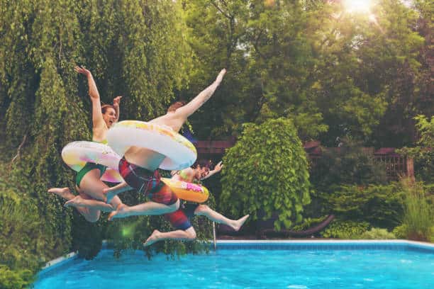 Famille qui saute dans sa piscine pendant les vacances à la maison